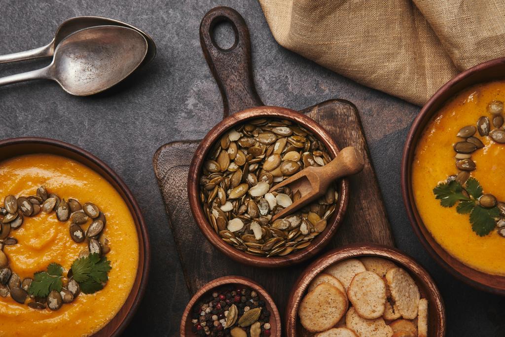 вид зверху на здорове гарбузове насіння, спеції, палички та смачний гарбузовий суп у мисках
 - Фото, зображення