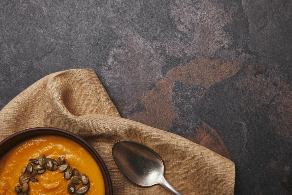 vista dall'alto di deliziosa zuppa di zucca con semi e cucchiaio su sacco su superficie scura
 - Foto, immagini