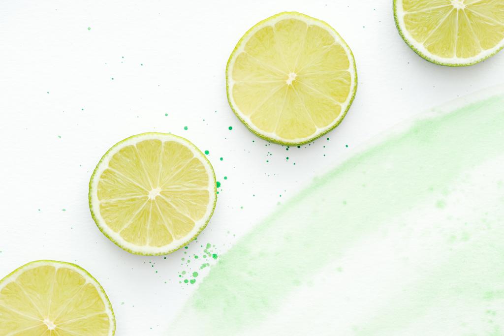 vue de dessus des morceaux de limes vives mûres sur la surface blanche avec aquarelle verte
 - Photo, image