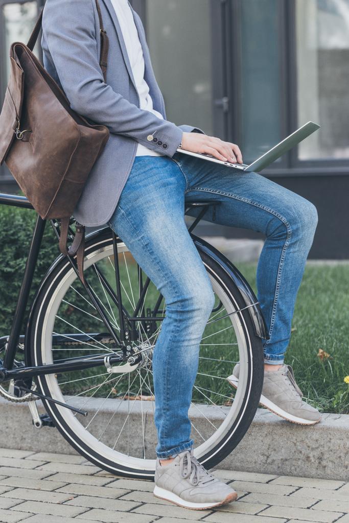 vista ritagliata di freelance con zaino in pelle che lavora su laptop mentre si siede in bicicletta
 - Foto, immagini