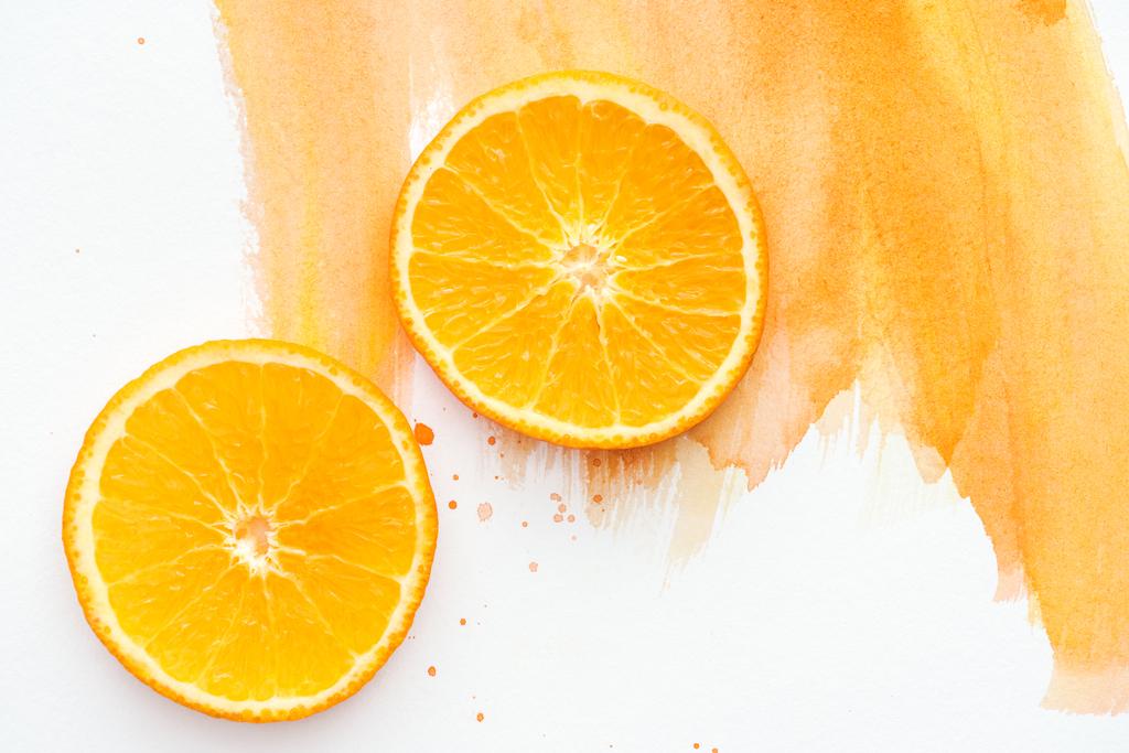 Ansicht von zwei reifen orangen Stücken auf weißer Oberfläche mit orangefarbenem Aquarell - Foto, Bild
