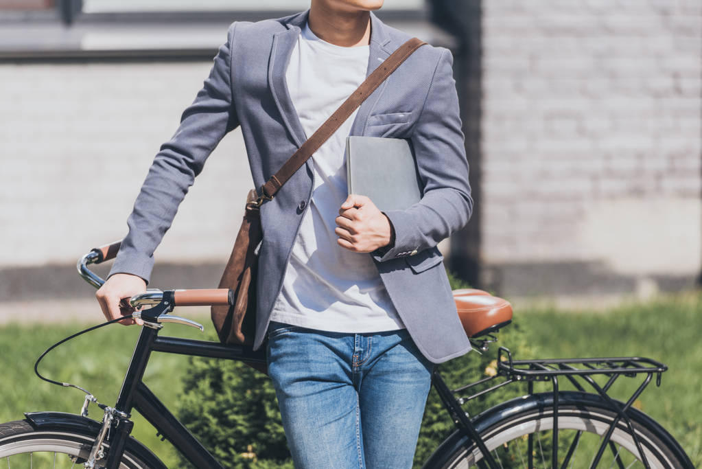 vue recadrée de l'homme élégant avec ordinateur portable et sac en cuir debout à vélo
 - Photo, image