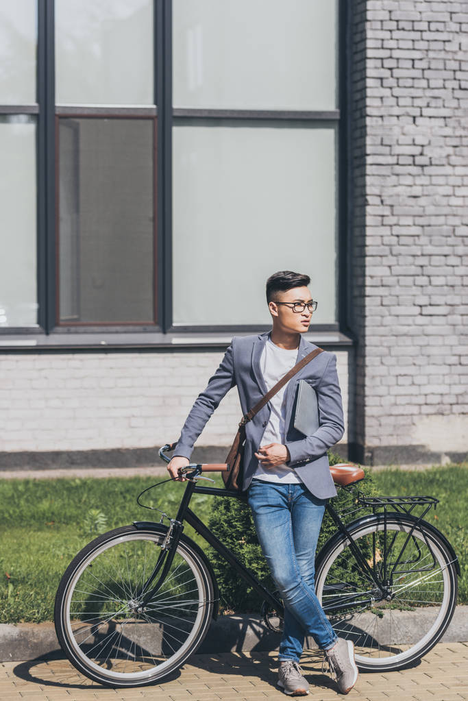 knappe zelfverzekerde Aziatische man met laptop staan op de fiets - Foto, afbeelding