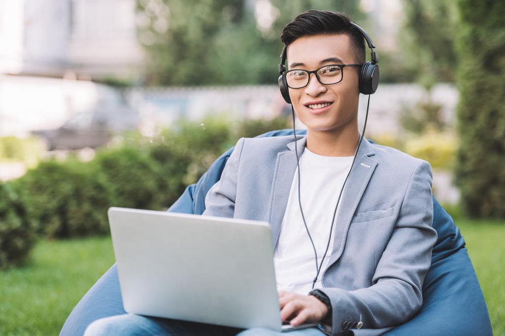 Aziatisch mens telewerken op laptop glimlachend zittend op bean bag stoel - Foto, afbeelding