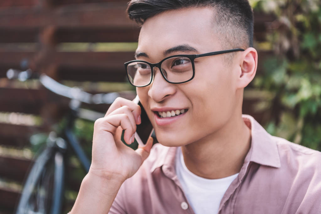 Lächelnder asiatischer Mann mit Brille spricht auf Smartphone - Foto, Bild