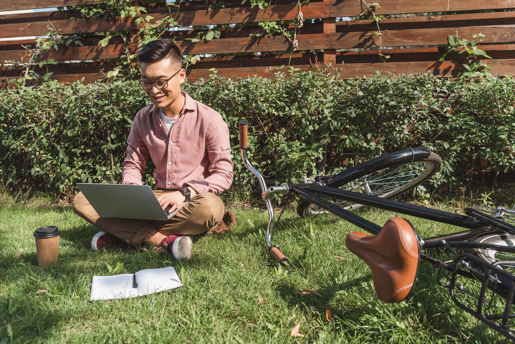 Aziatische freelancer werkt op laptop op groene gras met fiets- en notebook in park - Foto, afbeelding