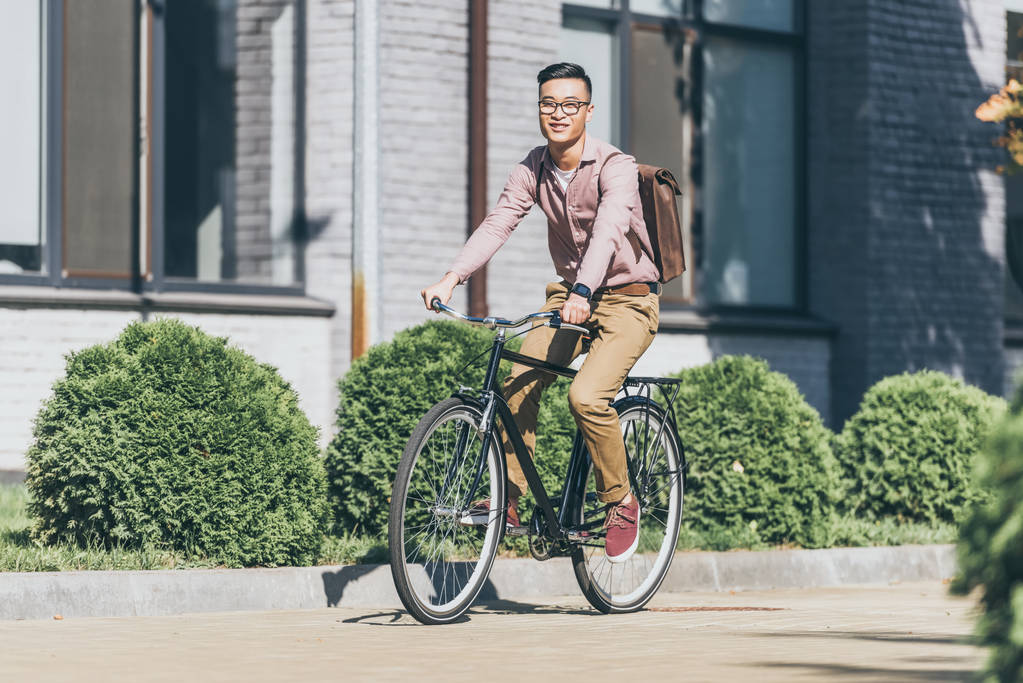  asian young man with backpack riding bicycle on street - Photo, Image