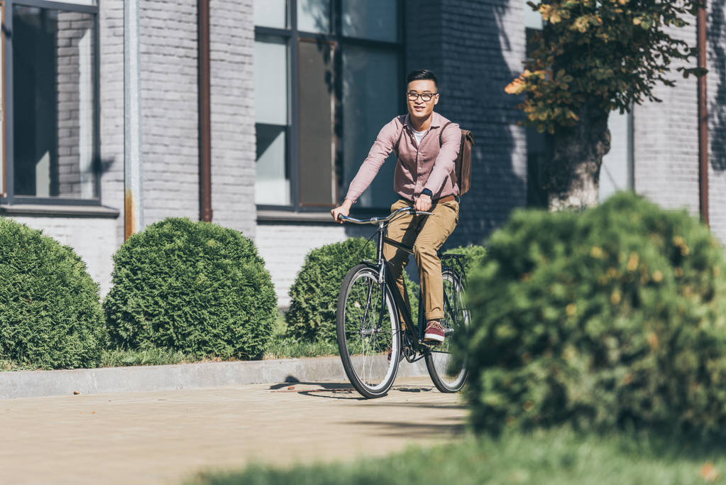  asian young man with backpack riding bicycle on street - Photo, Image