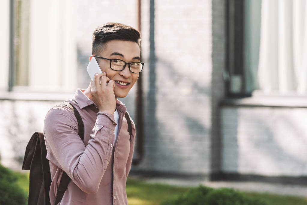  boční pohled na asijské mladý muž v brýlích s konverzaci na smartphone na ulici - Fotografie, Obrázek