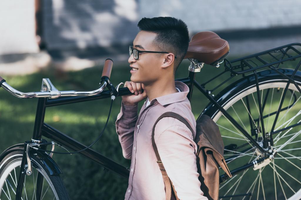  hymyilevä aasialainen mies kuljettaa polkupyörää kävellessään kadulla
 - Valokuva, kuva