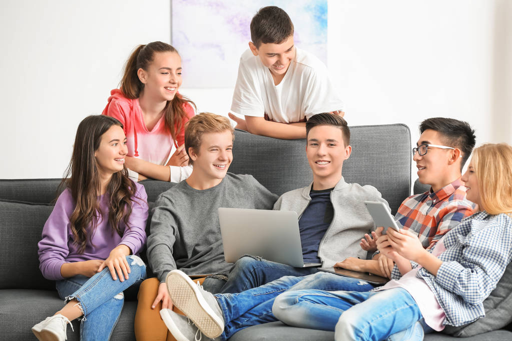 Gruppe von Teenagern mit modernen Geräten macht Selfie, während sie drinnen auf dem Sofa sitzen - Foto, Bild