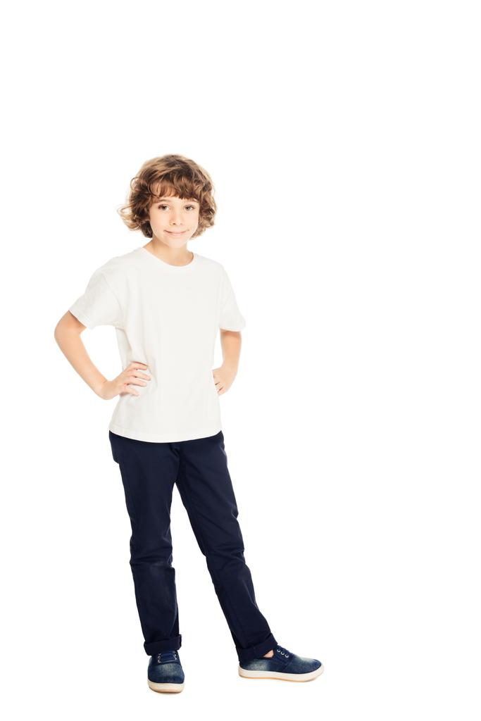 χαμογελώντας αξιολάτρευτο παιδί στέκεται με τα χέρια akimbo και πιο φωτογραφική μηχανή που απομονώνονται σε λευκό - Φωτογραφία, εικόνα