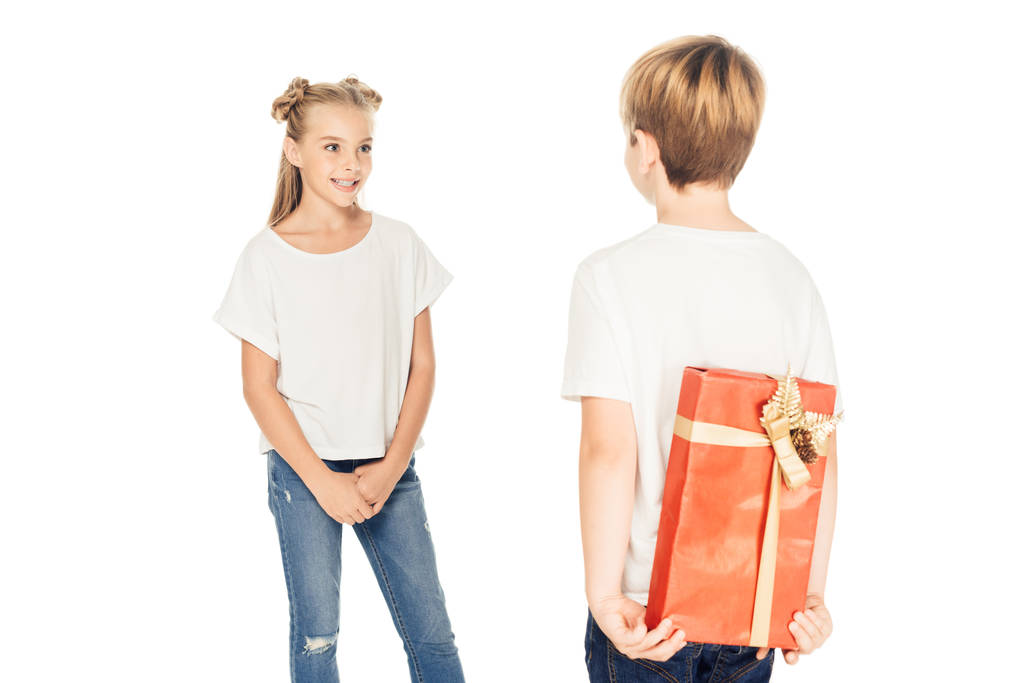 niño ocultando caja de regalo detrás de nuevo para presentar a un amigo aislado en blanco
 - Foto, imagen