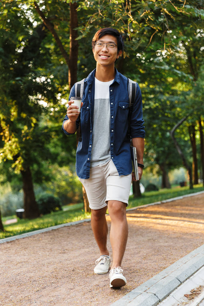 Täyspitkä kuva Happy aasialainen mies opiskelija silmälasit kävely kannettavan tietokoneen puistossa
 - Valokuva, kuva