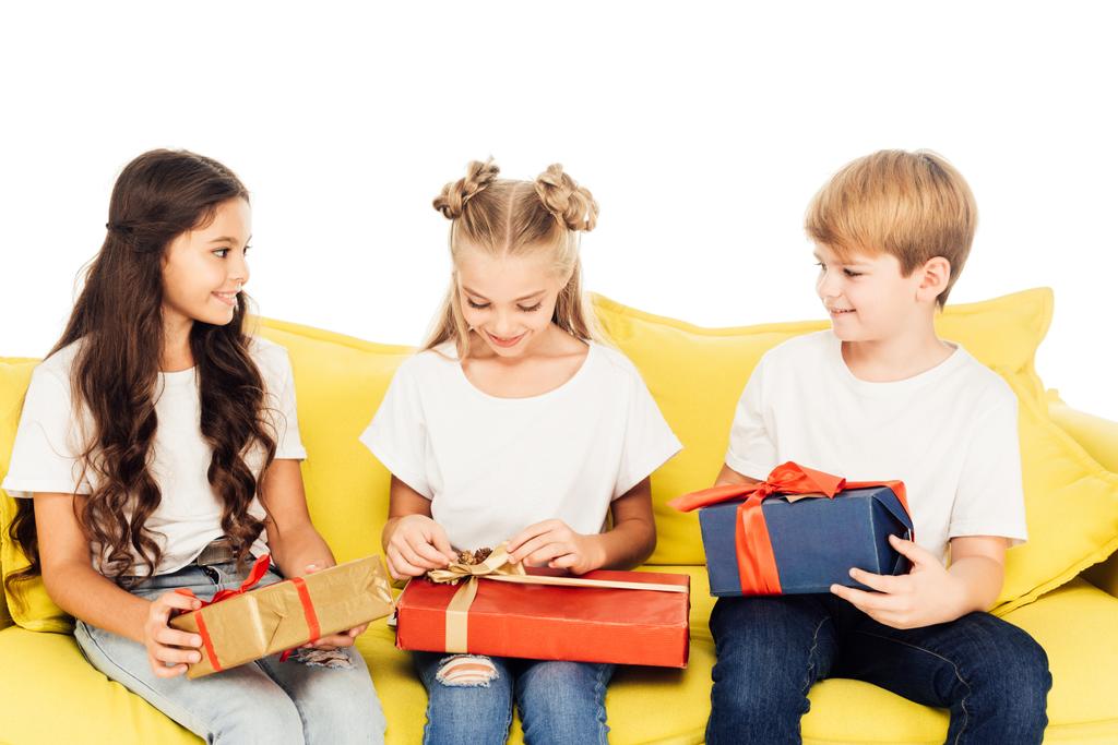 adorable kids sitting on yellow sofa and opening gift boxes isolated on white - Photo, Image