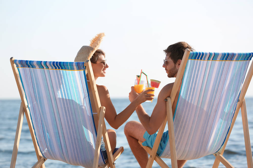 Jong (echt) paar met cocktails in strandstoelen op Zeekust - Foto, afbeelding