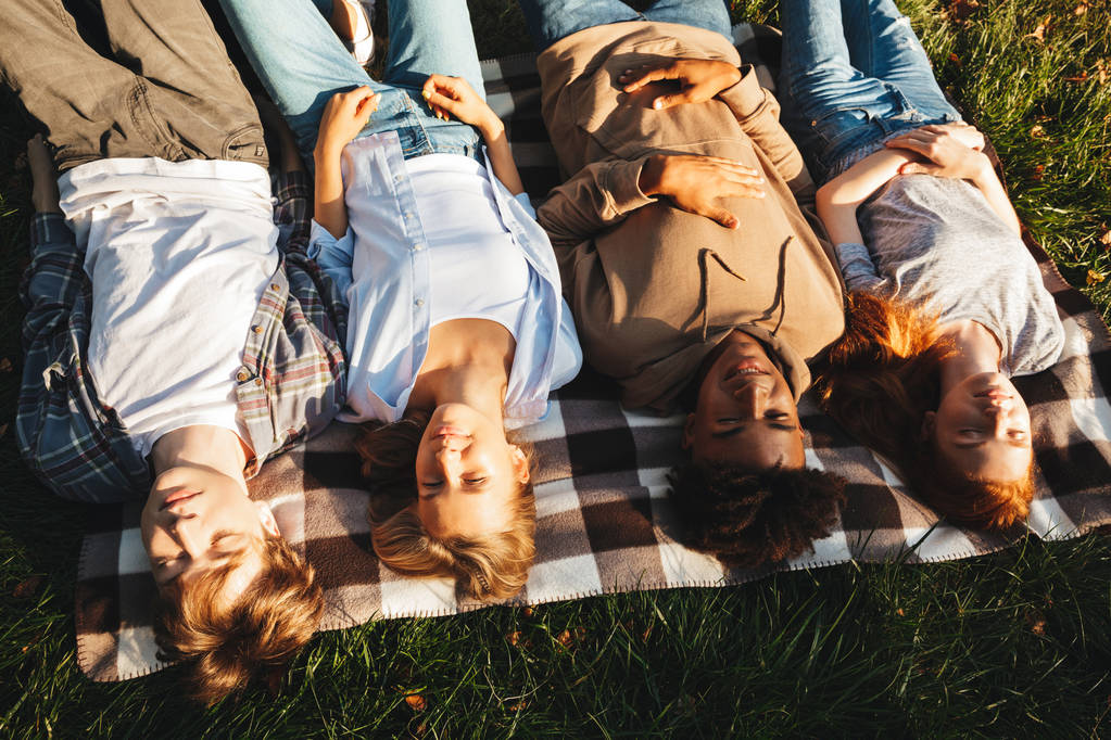 Visão superior do grupo de estudantes multhiethnic sorridentes que colocam em uma grama com os olhos fechados
 - Foto, Imagem