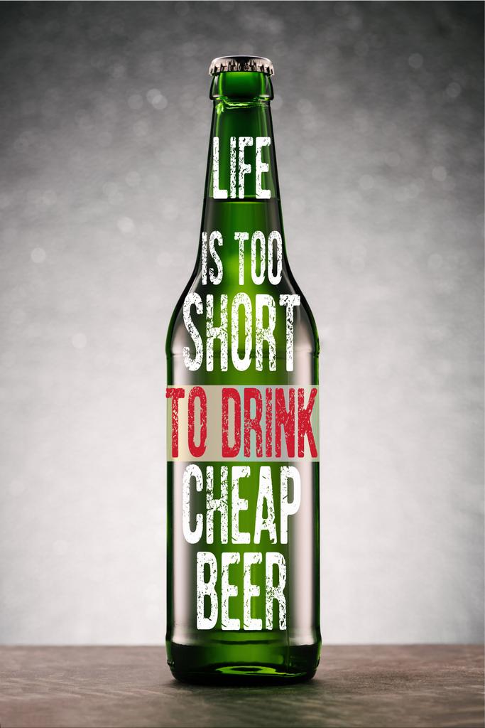 бутылка пива на столешнице на сером фоне с вдохновением "жизнь слишком коротка, чтобы пить дешёвое пиво"
  - Фото, изображение