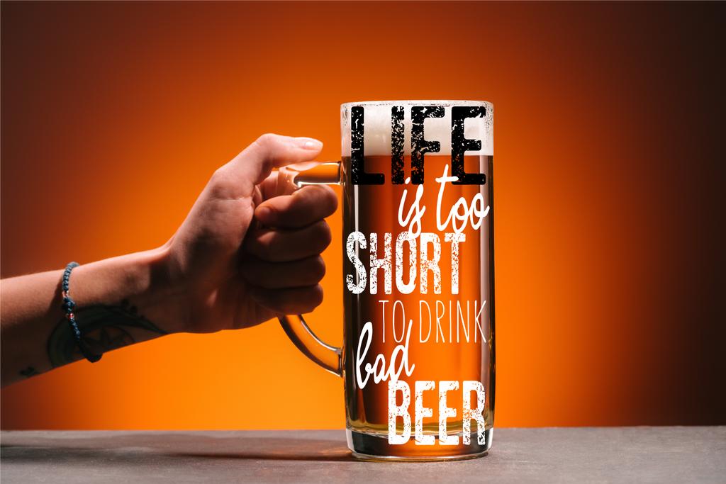 обрізаний знімок жінки, що тримає келих холодного пива з піною на помаранчевому тлі з натхненням "життя занадто коротке, щоб пити дешеве пиво"
 - Фото, зображення