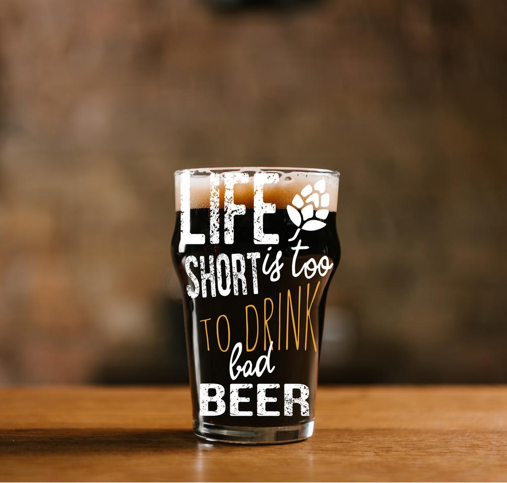 szklankę świeżego zimne piwo ciemne na drewnianym stole w pubie z inspiracji "życie jest zbyt krótkie, aby pić piwo tanie" - Zdjęcie, obraz