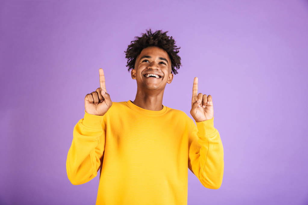 Portrait d'un jeune homme afro-américain joyeux vêtu de sweat-shirt pointant les doigts vers le haut isolé
 - Photo, image