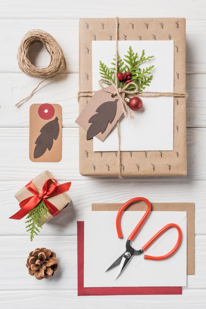 erhöhter Blick auf arrangierte Weihnachtsgeschenkboxen, Christbaumkugeln und immergrüne Kegel auf Holztisch - Foto, Bild