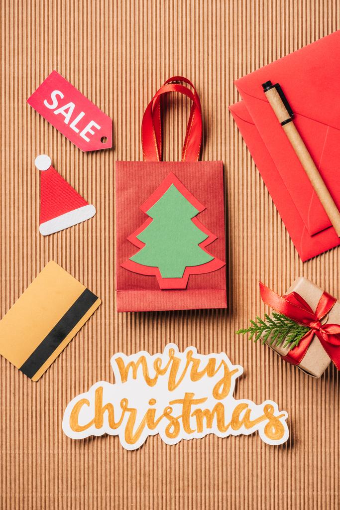 vista superior do saco de compras vermelho, caixa de presente decorada, cartão de crédito e letras Feliz Natal na superfície
  - Foto, Imagem