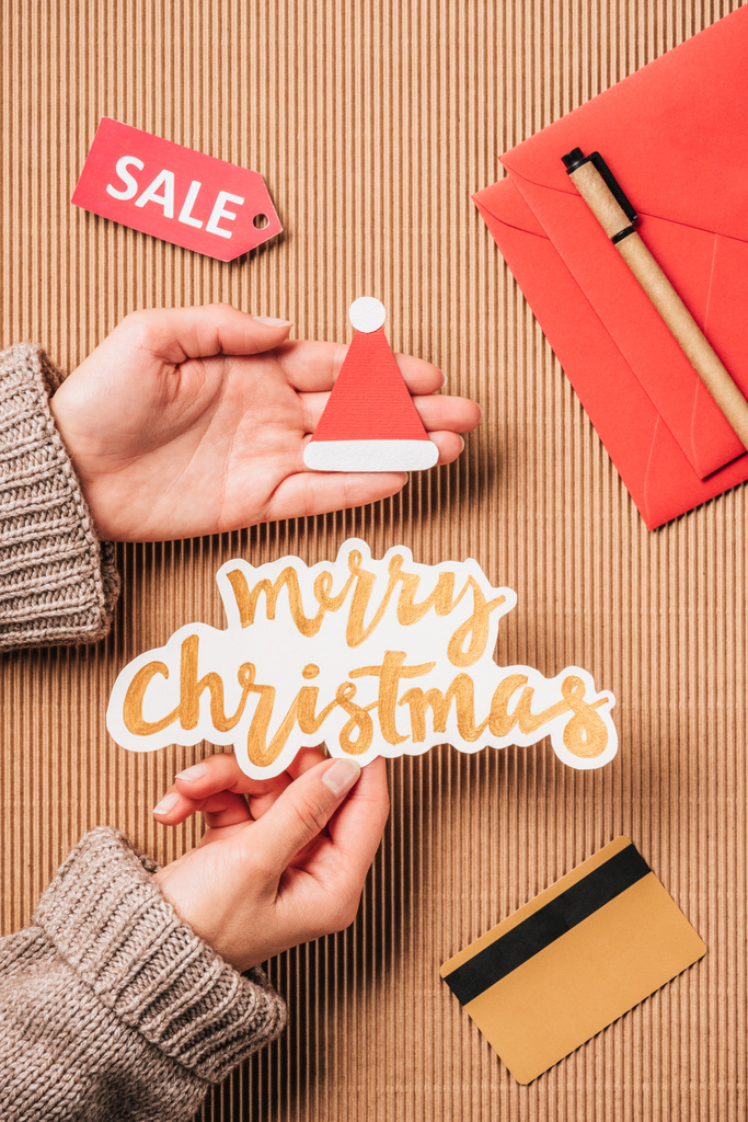 zugeschnittenes Bild einer Frau mit frohem Weihnachten Schriftzug und Weihnachtsmütze über der Oberfläche mit Kreditkarte und Verkauf  - Foto, Bild