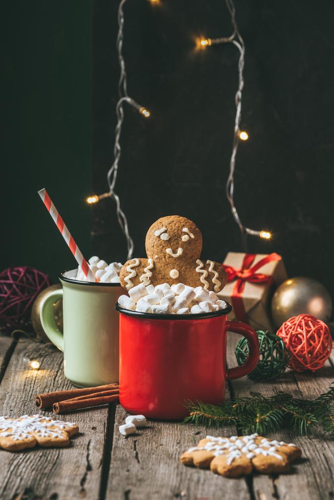 дві чашки какао з зефіром і імбирним чоловіком на дерев'яному столі з різдвяною світлою гірляндою
 - Фото, зображення