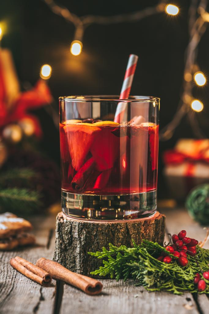 copo de vinho quente no toco de madeira com paus de canela e grinalda de luz de Natal
 - Foto, Imagem
