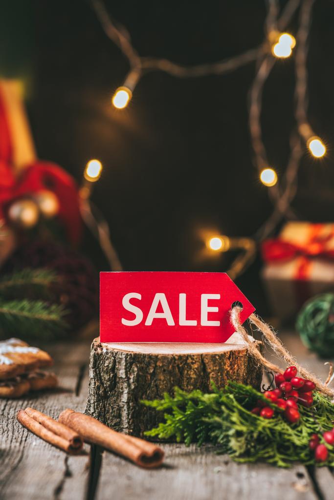 etiqueta de venta de Navidad roja en tocón de madera con palos de canela y guirnalda ligera
 - Foto, Imagen