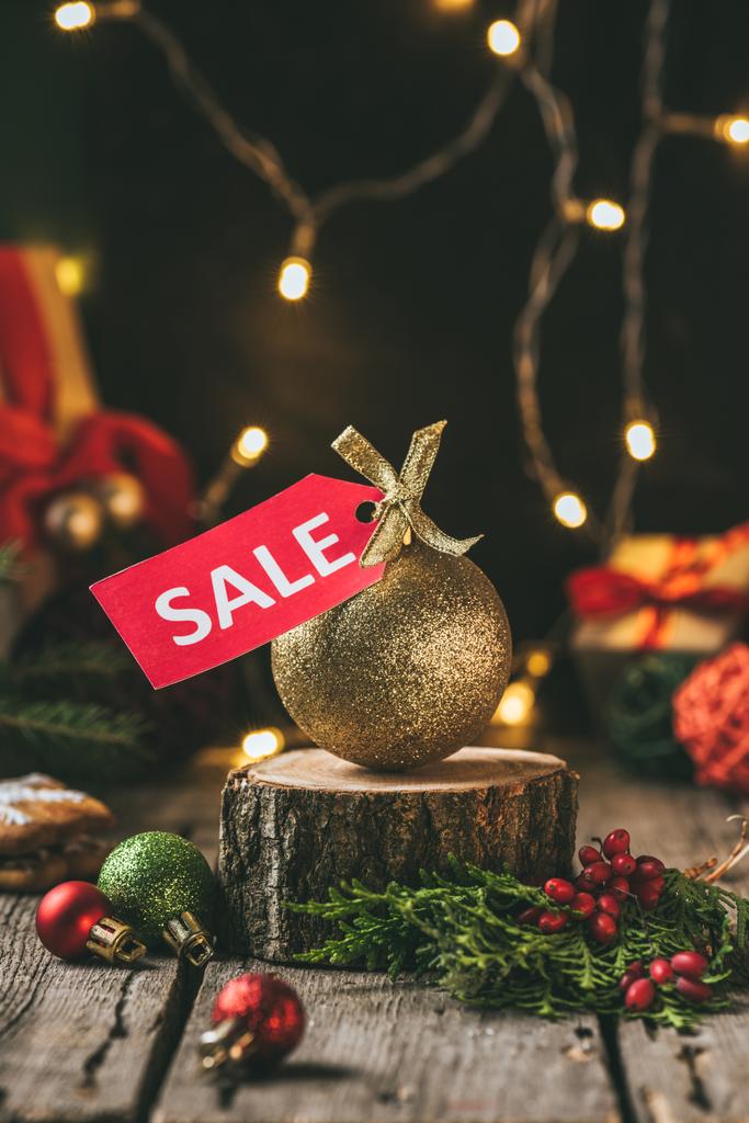 Golden karácsony labdát vörös eladó tag a fa stump, a fény koszorú - Fotó, kép