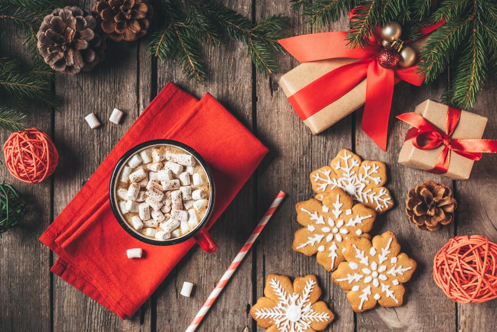 вид сверху на пряники, рождественские подарки и чашку какао с зефиром на деревянном фоне с елкой
 - Фото, изображение