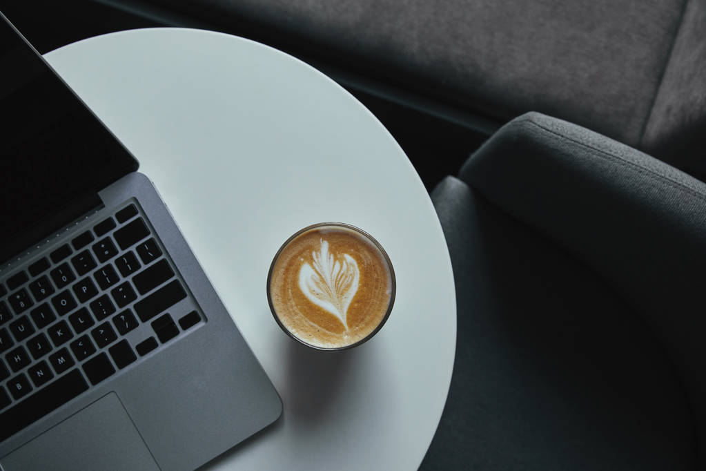 Draufsicht auf eine Tasse Cappuccino und einen Laptop auf einem Tisch im Café  - Foto, Bild