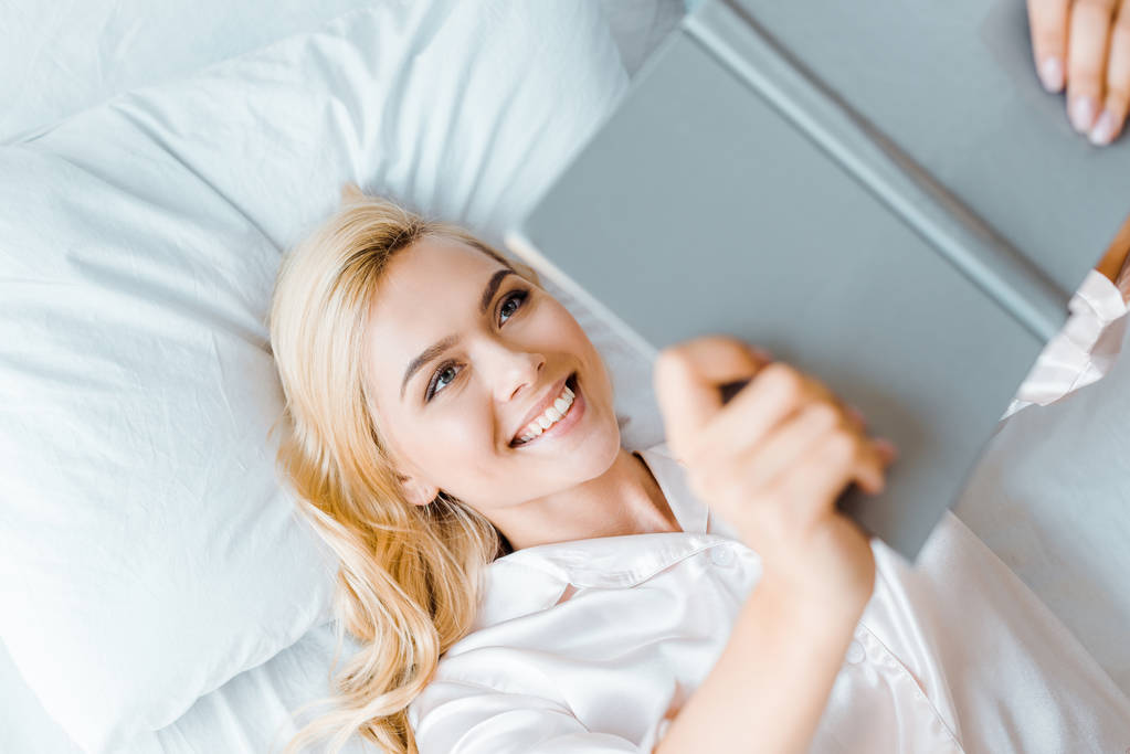 vista superior da jovem mulher feliz deitada na cama e livro de leitura
 - Foto, Imagem
