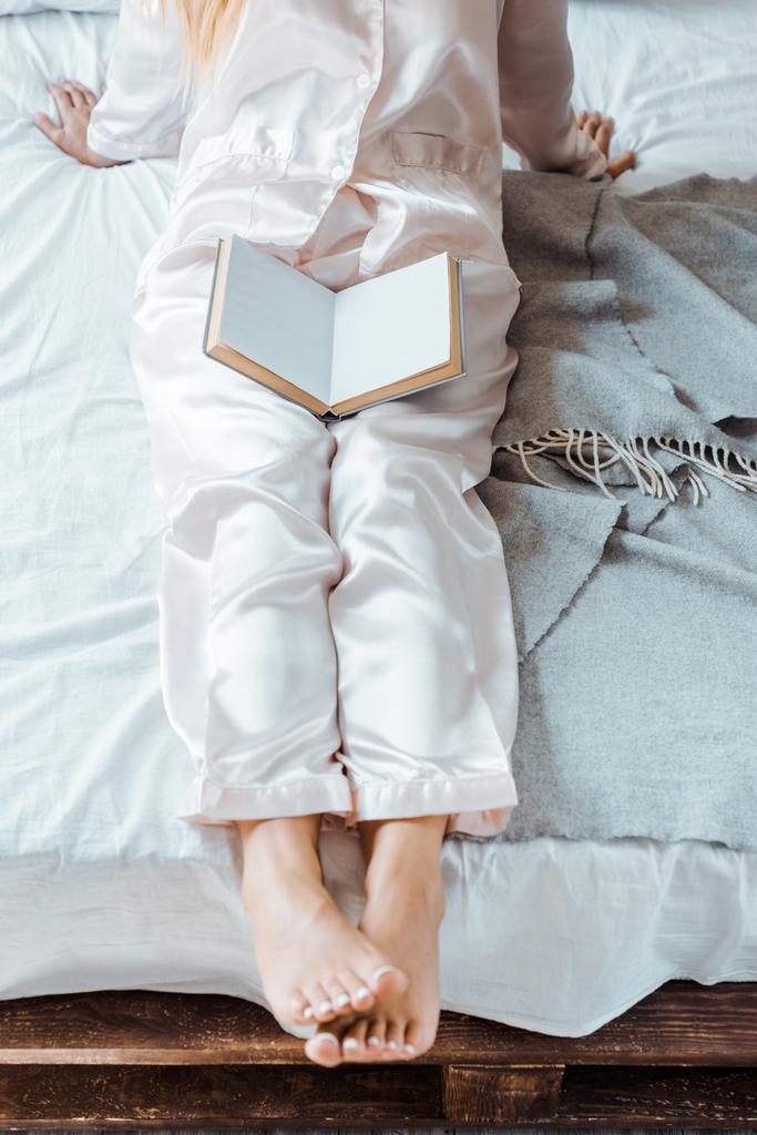 περικοπεί shot νεαρή γυναίκα στο πιτζάμες κάθεται στο κρεβάτι με το βιβλίο - Φωτογραφία, εικόνα