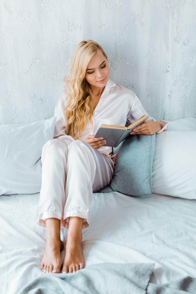 високий кут зору красива молода жінка в піжамі сидить на ліжку і читає книгу
 - Фото, зображення