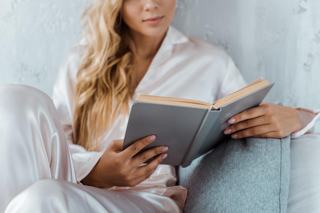 ベッドの上に座って、本を読んではパジャマ姿で若い女性のクロップ撮影 - 写真・画像