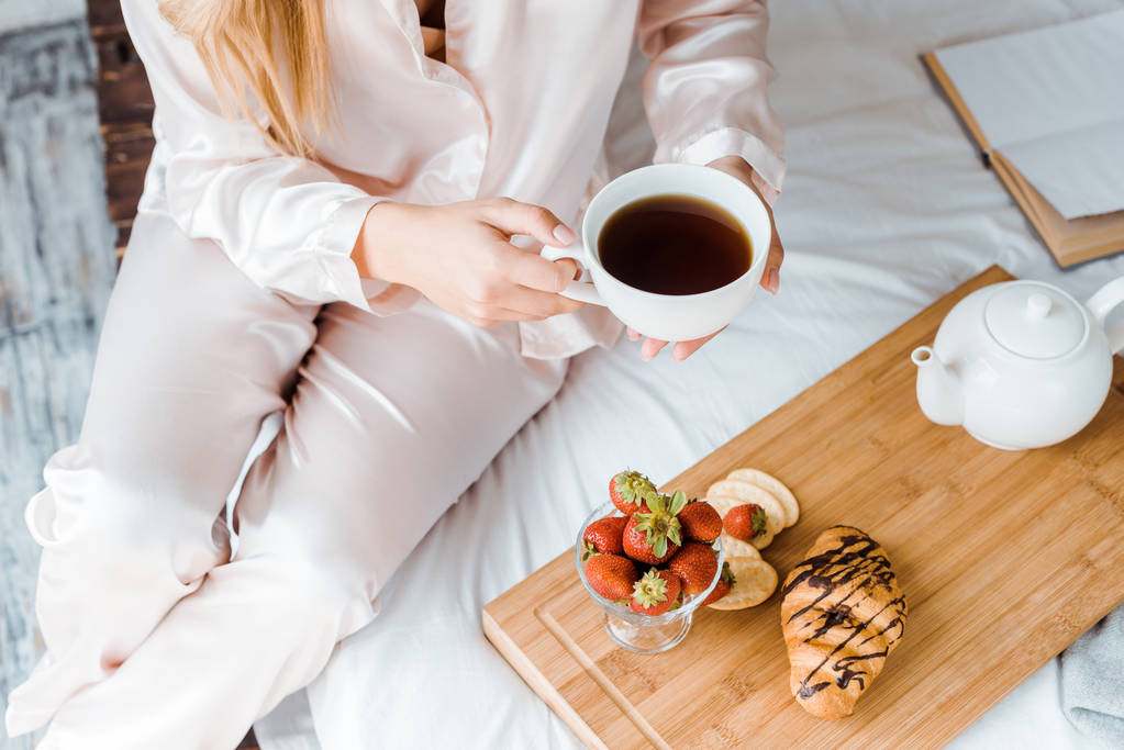 imagem cortada de mulher em pijama segurando xícara de chá na cama de manhã
 - Foto, Imagem