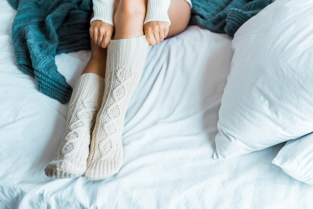 bijgesneden afbeelding van vrouw in trui dragen van gebreide beenkappen in slaapkamer in ochtend - Foto, afbeelding