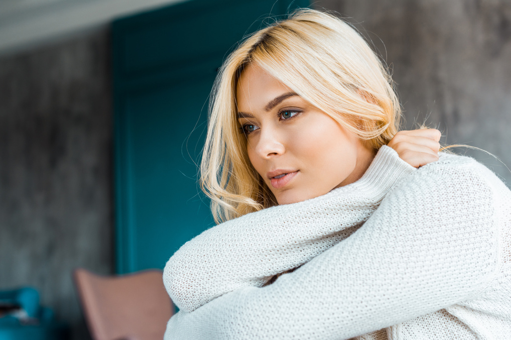 pensive attractive woman in sweater looking away in bedroom in morning - Photo, Image