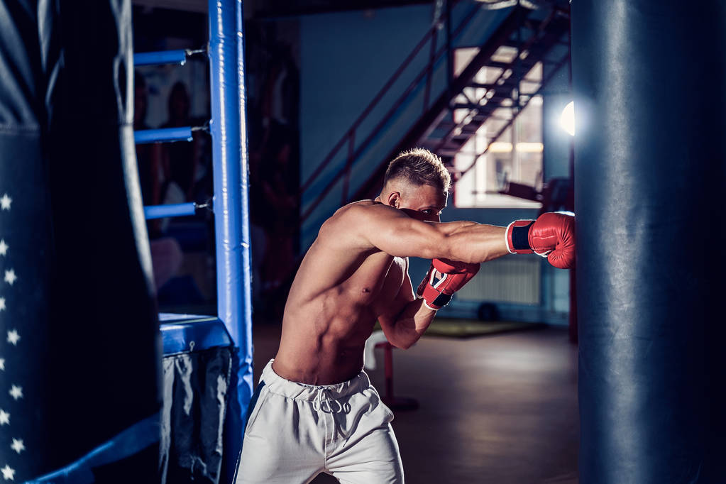 Allenamento pugile maschile con sacco da boxe nel palazzetto dello sport scuro. - Foto, immagini
