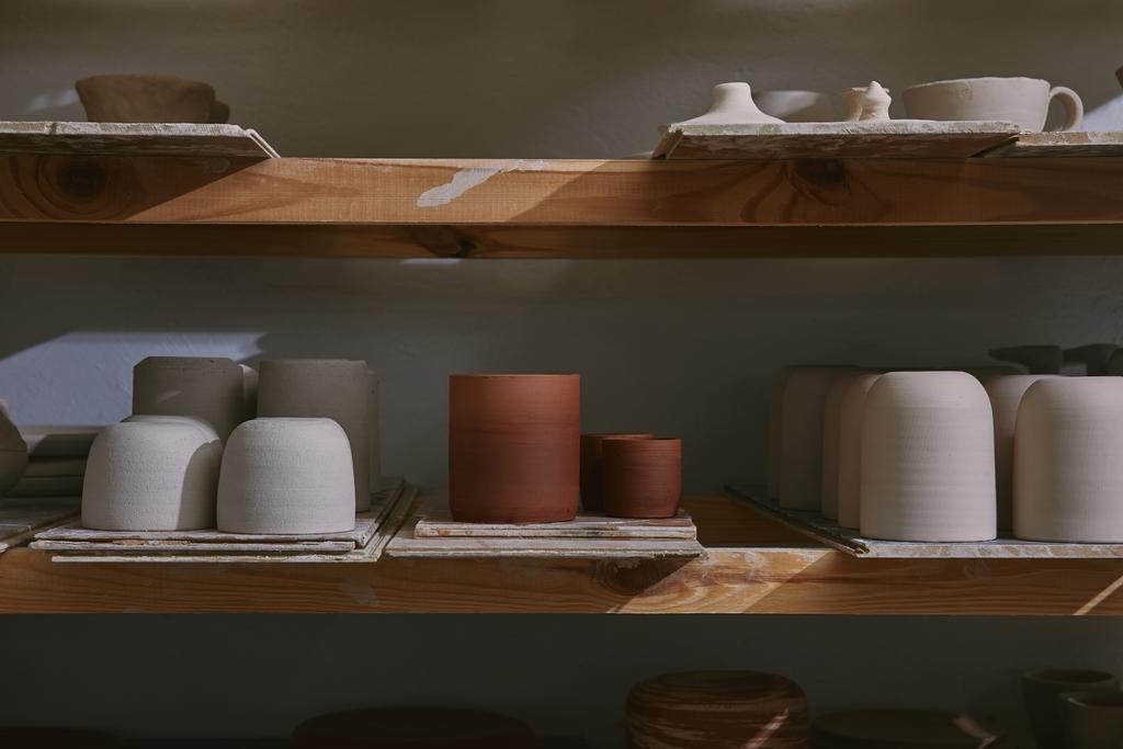 κεραμικά κύπελλα και πιάτα πάνω σε ξύλινα ράφια στο εργαστήριο κεραμικής - Φωτογραφία, εικόνα