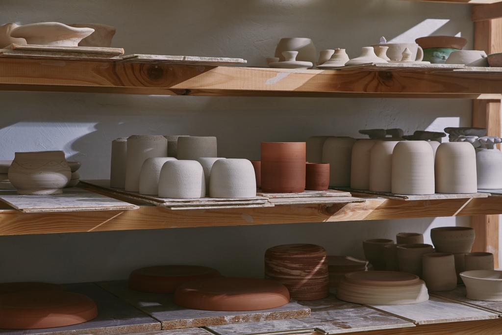 tigelas de cerâmica e pratos em prateleiras de madeira no estúdio de cerâmica
 - Foto, Imagem