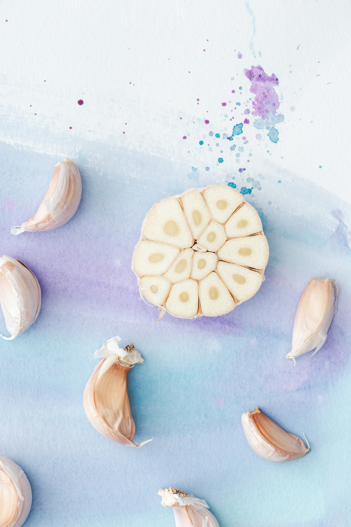 top view of sliced garlic on white surface with purple watercolor strokes - Photo, Image