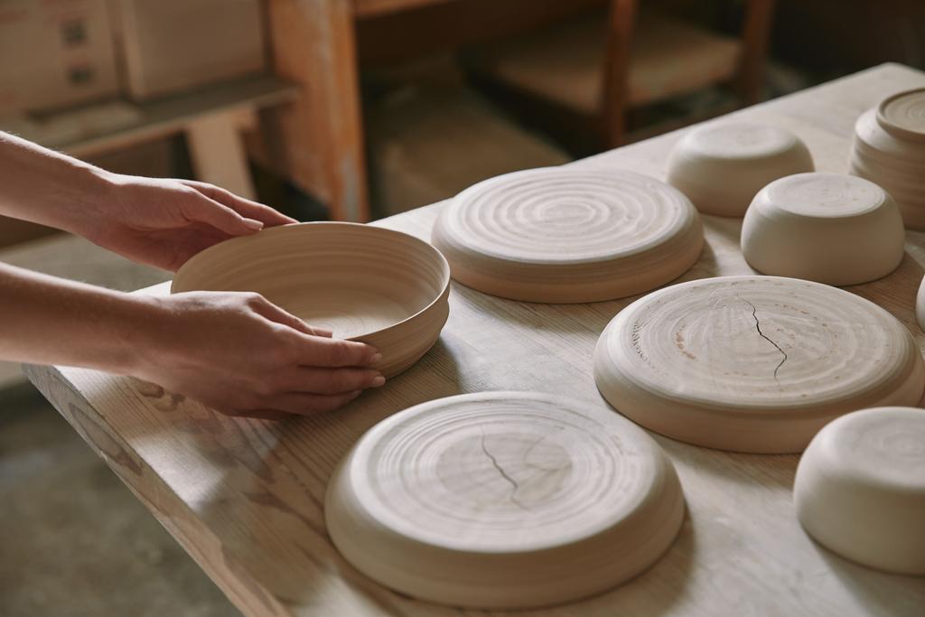 partial view of woman putting ceramic dish on table at workshop - Photo, Image
