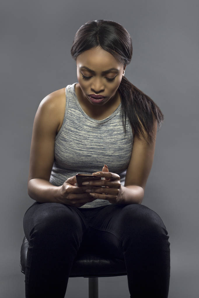 schwarze Sportlerin mit Smartphone-Fitness-App, die besorgt auf Trainingsdaten schaut oder durch das Lesen von Textnachrichten vom Training abgelenkt wird - Foto, Bild