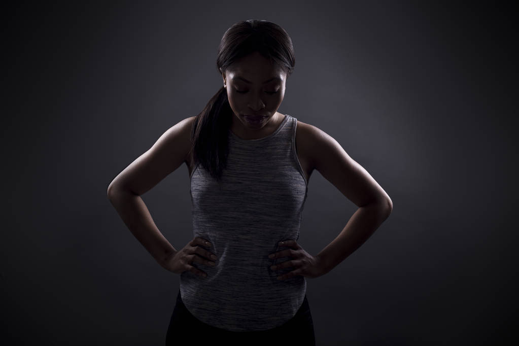Силуэт черной женщины в злой позе или портрет спортсмена, концентрирующегося на экстремальных спортивных соревнованиях. Лицо в тени, чтобы изобразить гнев или ярость
. - Фото, изображение