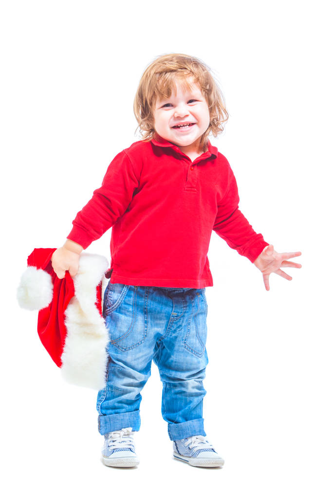 Natale. Un bambino con un cappello da Babbo Natale, con giacca rossa e jeans blu. Isolato su sfondo bianco
. - Foto, immagini