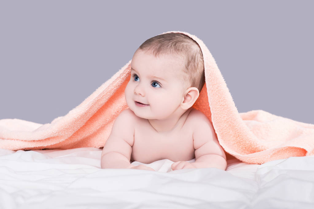 赤ん坊シャワー、灰色の背景の上分離後ピンクのタオルの下の腹の上に横たわる大きな青い目を - 写真・画像